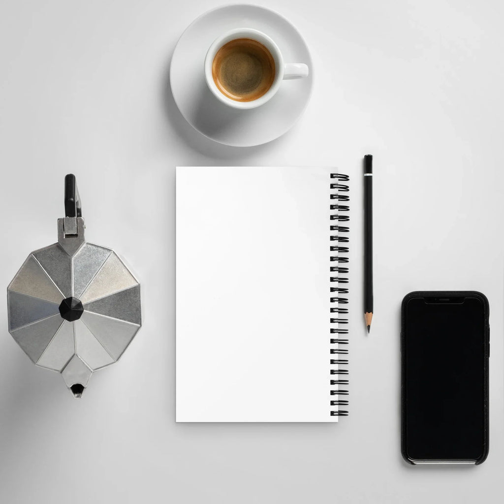 Carnet à spirale blanc sur bureau avec stylo, tasse de café, cafetière et smartphone.