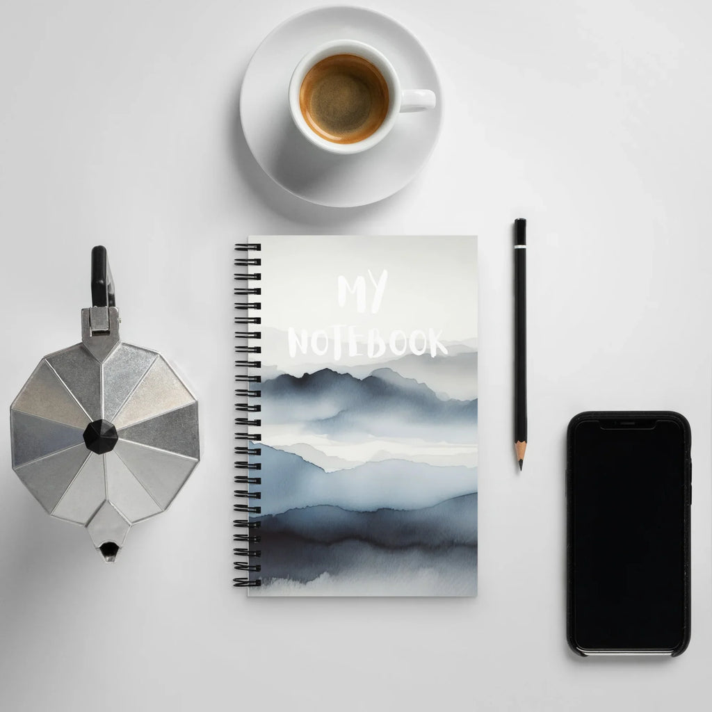 Carnet à spirale motif montagnes, avec tasse de café, crayon, cafetière et smartphone.